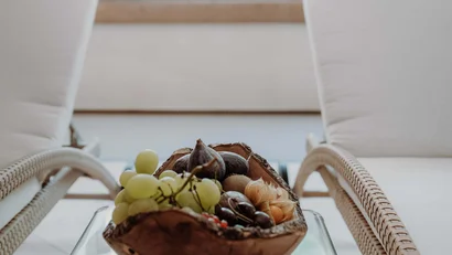 Obstschale mit Trauben und Feigen auf Glastisch zwischen zwei weißen Stühlen