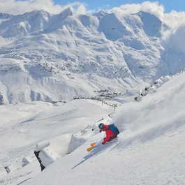 Skifahrer fährt steil den schneebedeckten Berg hinunter mit Alpen im Hintergrund