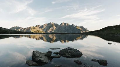 Bergspitzen spiegeln sich in einem ruhigen See unter klarem Himmel