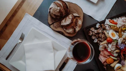 Wooden board with bread, plate with napkin, glass of red wine and appetizer platter