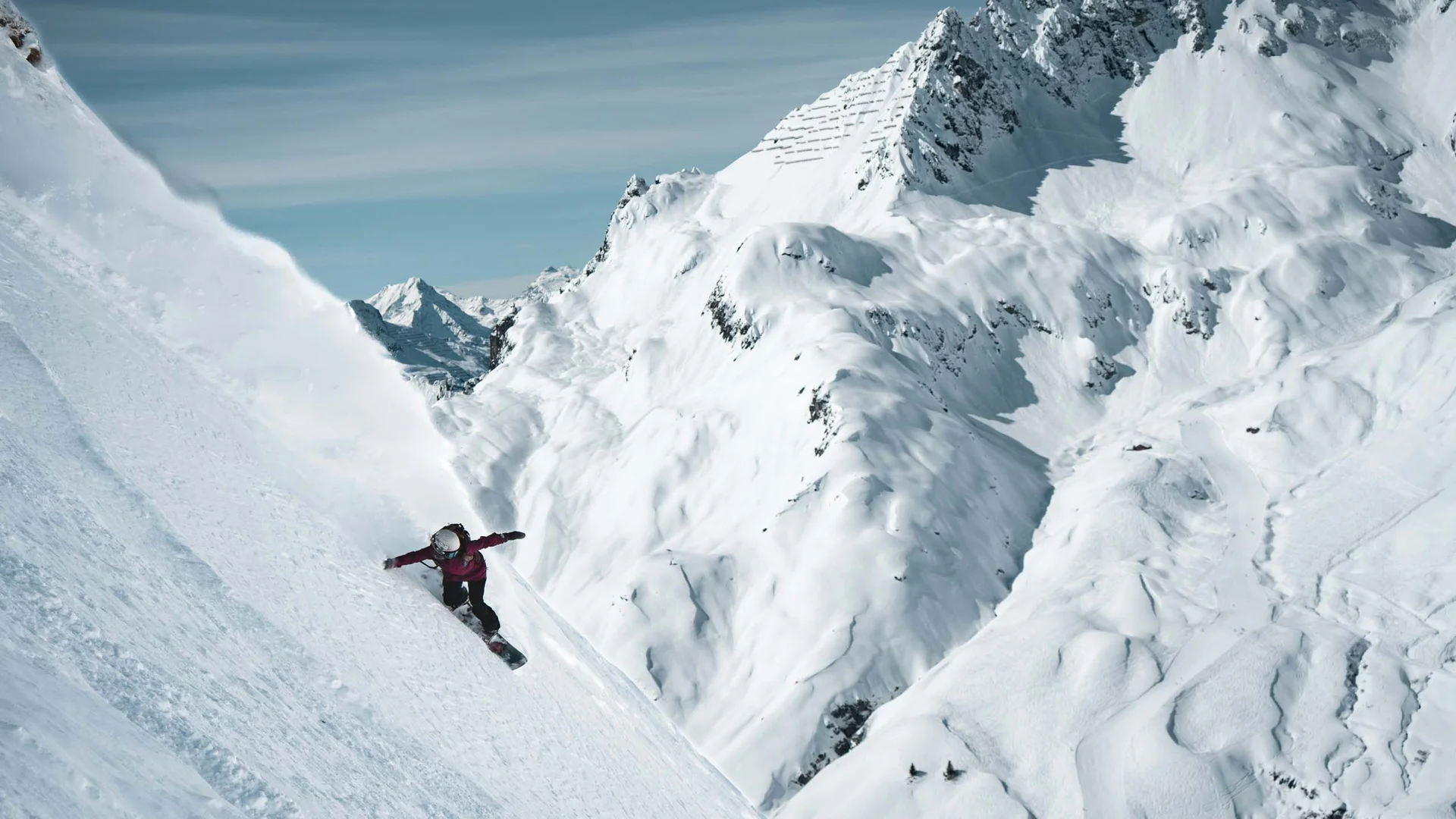 Snowboarder descending steep snow-covered mountain slope