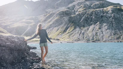 Frau wandert barfuß an einem klaren Bergsee mit felsiger Küste