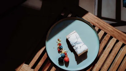 Stück Kuchen mit Puderzucker und Beeren auf blauem Teller auf Holzstuhl