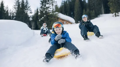 Kind und Erwachsene rodeln gemeinsam auf Schneehügel im Winterwald