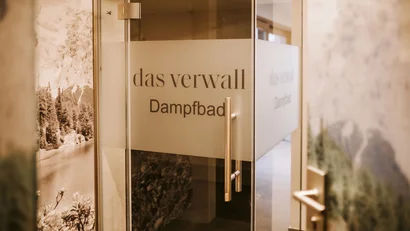 Glass door labeled Das Verwall steam bath in a bright room