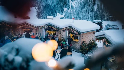 Verschneiter Weihnachtsmarkt mit beleuchteten Hütten und Menschen im Winter