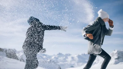 Zwei Personen im Schnee, eine wirft Schneebälle auf die andere in den Bergen