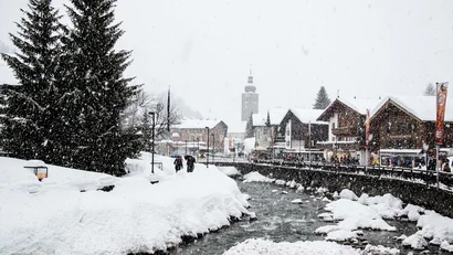 Schneebedecktes Dorf mit Fluss, Bäumen und Menschen unter schneefall