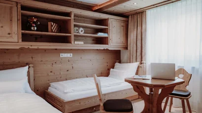 Kleines Holz-Zimmer mit Betten, Tisch, Stühlen und Laptop am Fenster