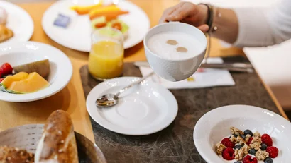 Various breakfast dishes and a hand holding a cup of coffee with milk foam