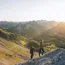 Two hikers climbing a steep mountain slope at sunset in a rugged mountain range