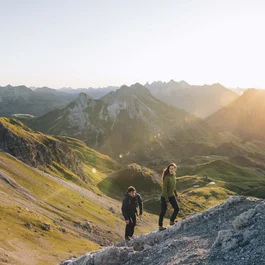 Two hikers climbing a steep mountain slope at sunset in a rugged mountain range