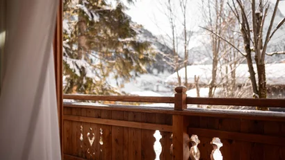 Blick von einem Balkon mit Holzgeländer auf schneebedeckte Bäume und Berge