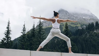 Frau macht Yoga-Pose auf Betonblöcken vor Bergkulisse