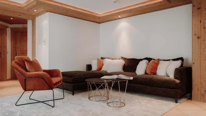 Gemütliche Sitzecke mit braunem Sofa und orangefarbenem Sessel in holzverkleidetem Raum