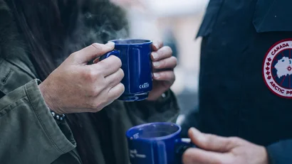 Zwei Personen halten dampfende blaue Tassen in kalter Umgebung