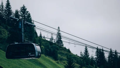 Seilbahn über grünem Hügel mit Kiefern und bewölktem Himmel