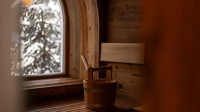 Holzsauna mit Eimer auf Bank und verschneitem Baum draußen