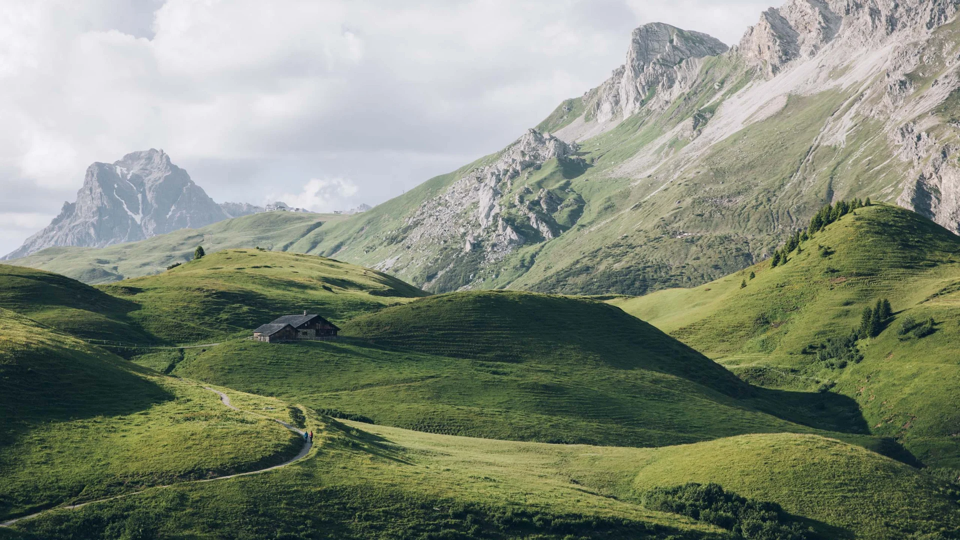 Grüne Hügel und Berge mit Hütte unter bewölktem Himmel
