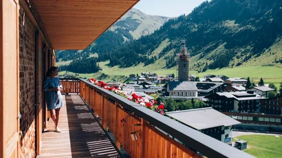 Frau auf Balkon mit Blick auf Dorf und Berge bei sonnigem Wetter