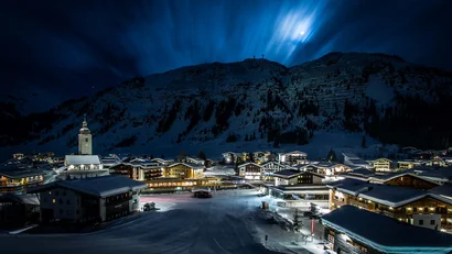 Dorf bei Nacht mit schneebedeckten Häusern und Berg im Hintergrund unter Mondlicht