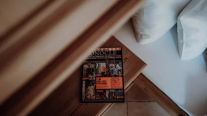 Zeitschrift auf Holzbank neben Bett mit weißen Kissen