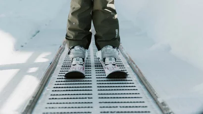 Kind in Skibekleidung mit Helm steht auf Förderband im Schnee