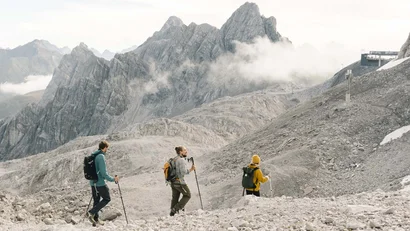 Drei Wanderer mit Rucksäcken und Stöcken in felsiger Berglandschaft