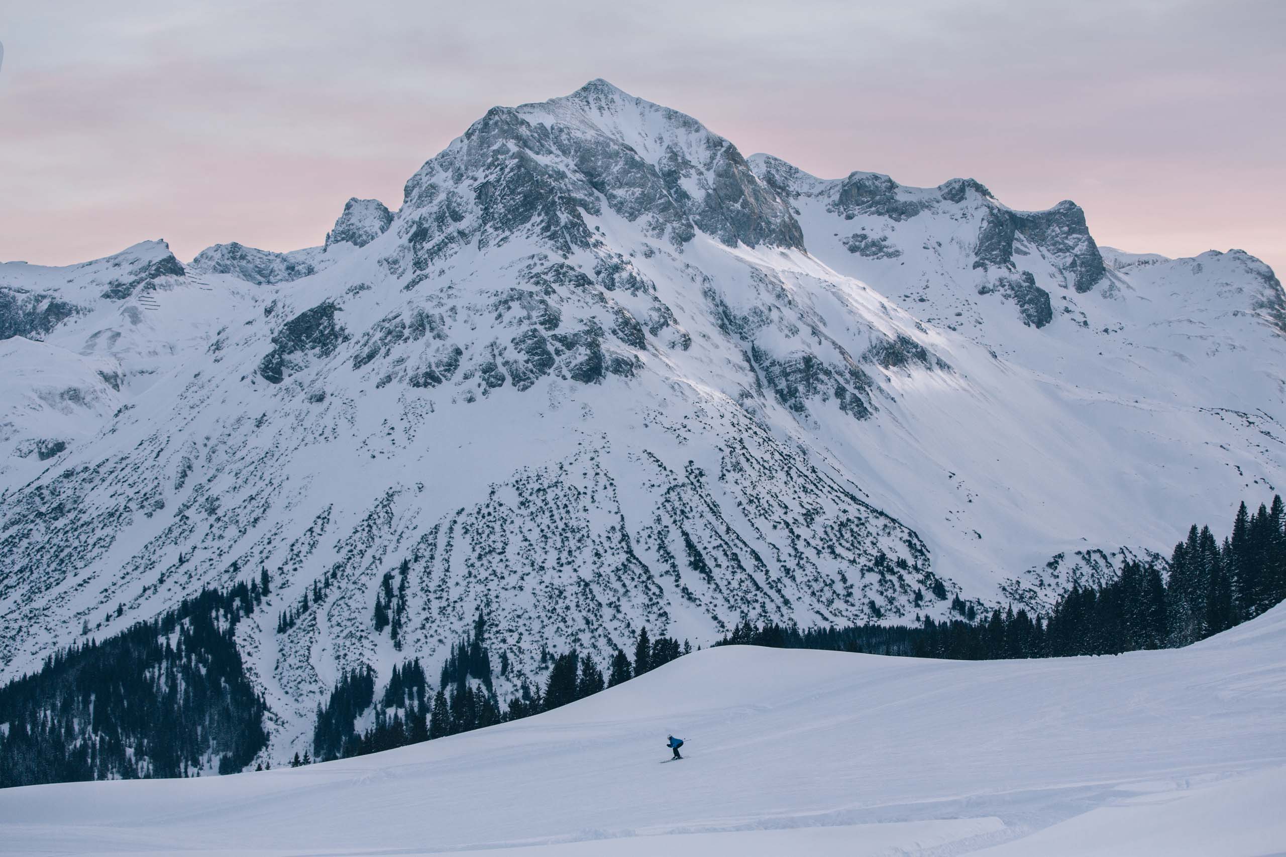 Skifahrer vor schneebedecktem Berg bei Abenddämmerung