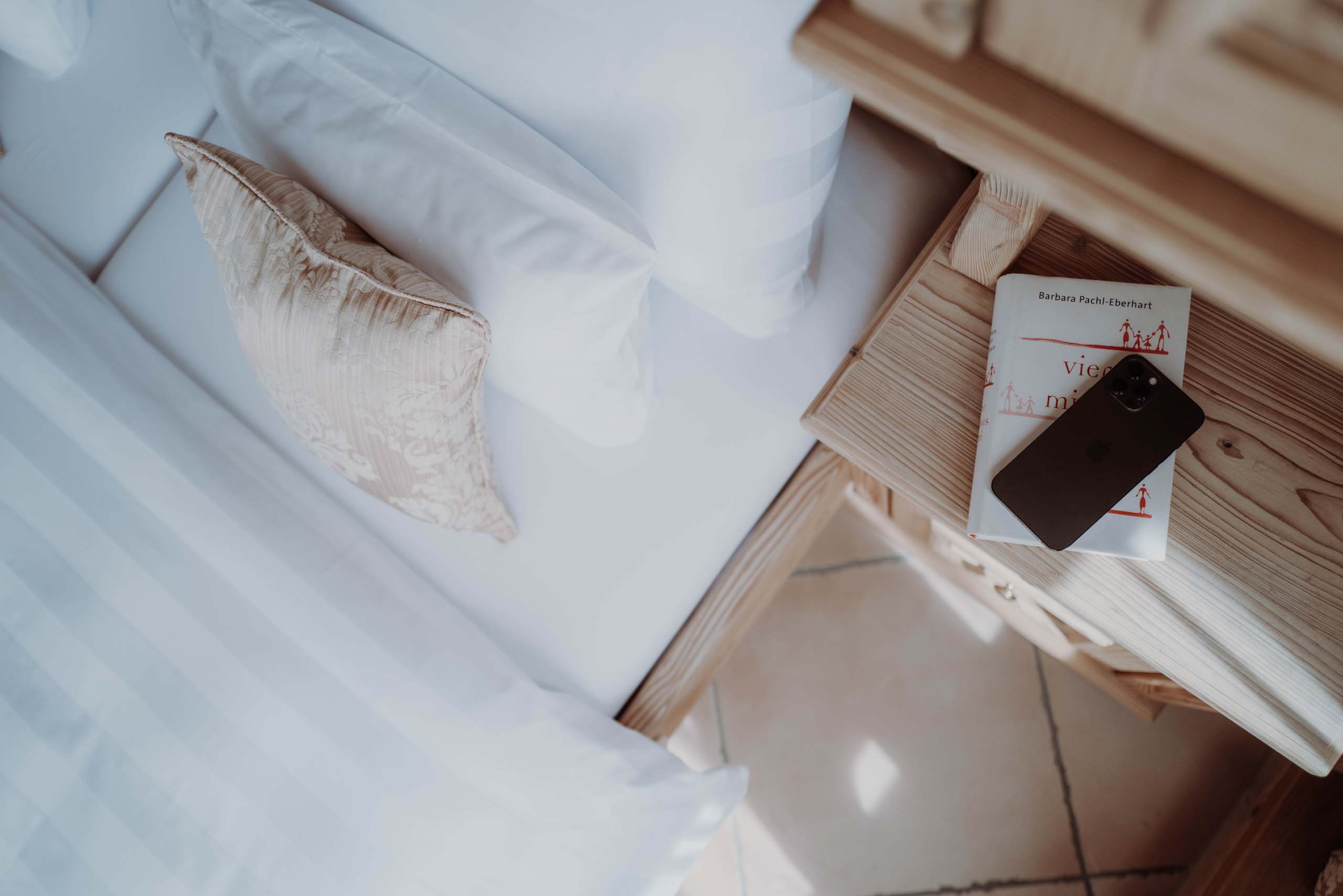Das Verwall | Finest Apartments in Lech am Arlberg Bett mit Kissen und Nachttisch mit Buch und Smartphone